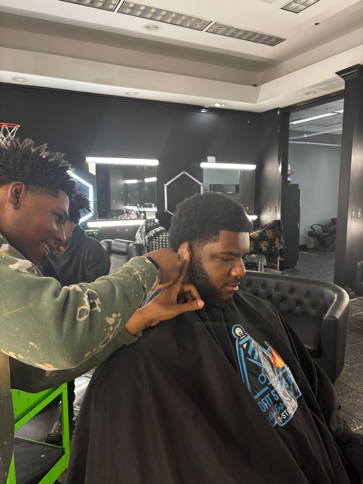 A barber working on a client's hairline while the client sits caped in the chair.