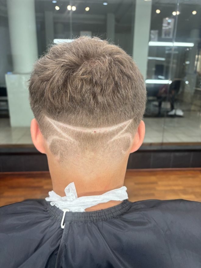 The back of a light blond taper with a curved design line shaved through the side.